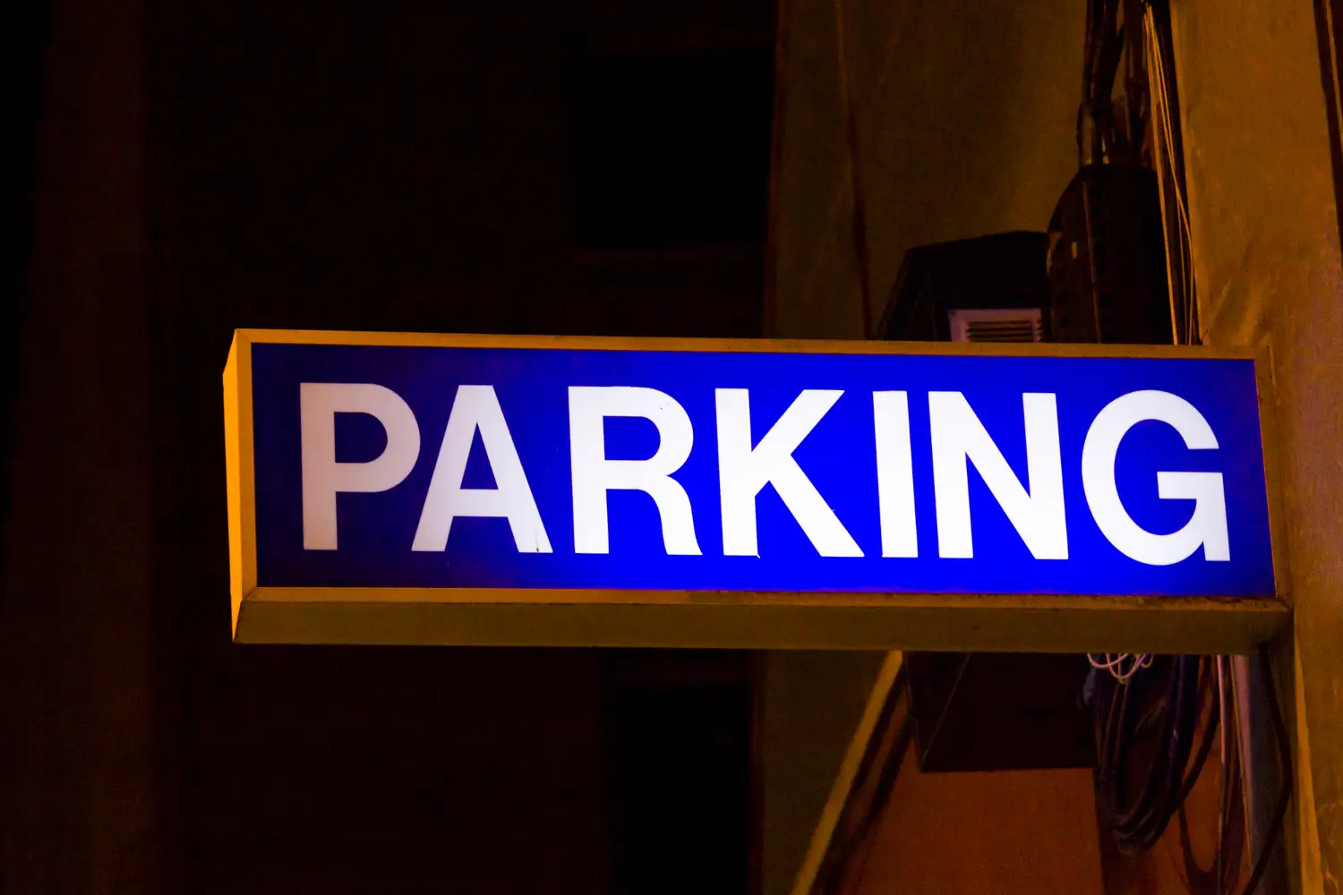Panneau lumineux bleu indiquant "PARKING" la nuit.